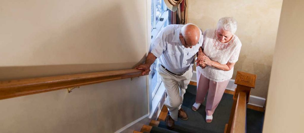 An elderly woman helps an elderly man climb a staircase.