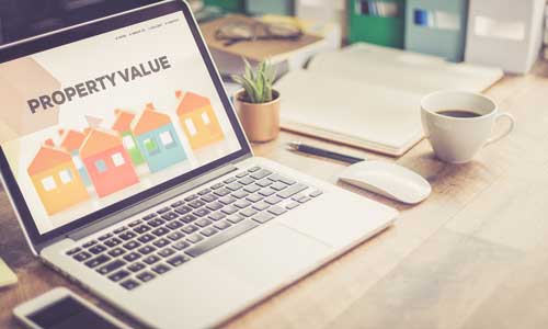 A laptop on a desk. On the screen is a webpage with the title "Property Value."