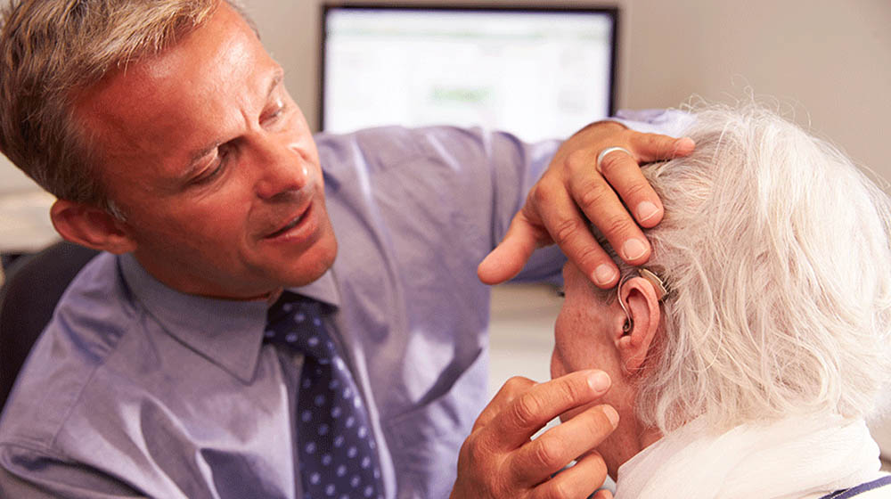 Feature image audiologist fits hearing aid on elderly woman